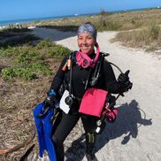 Kaitlyn Fay in scuba gear, smiling, carrying fins near the water